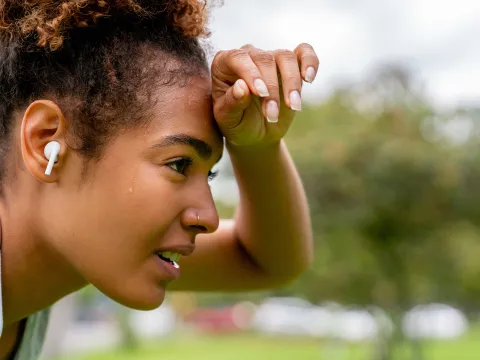 A woman wipes her brow while taking a break from exercising outdoors.