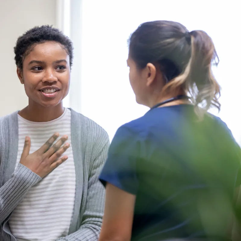 woman with hand over chest talking with doctor