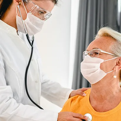 Masked doctor listening to lungs of masked caucasion female pateint with stethoscope