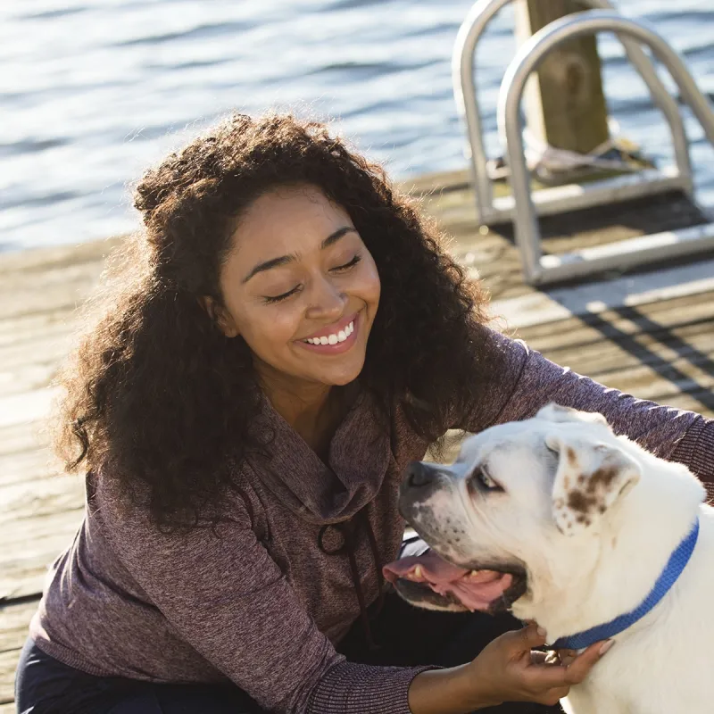 A young African American women plays with her dog on a dock by the lake.