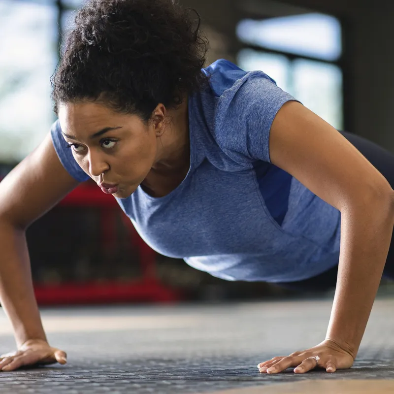 A young African American woman performs push-ups at the gym.