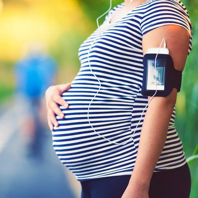 A pregnant woman rubs her belly while taking a break on a running trail.