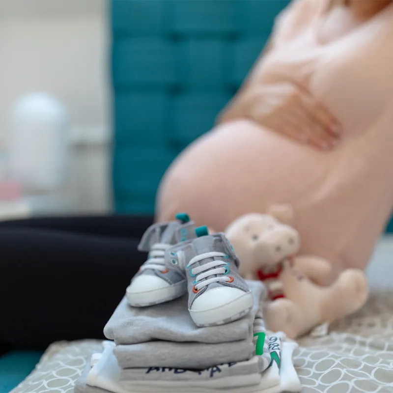 A picture of a set of baby clothes folded next to a pregnant mother