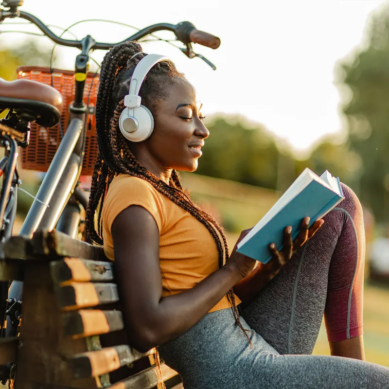 A Woman Takes a Break From Riding Her Bike By Sitting on a Park Bench and Reading a Book.