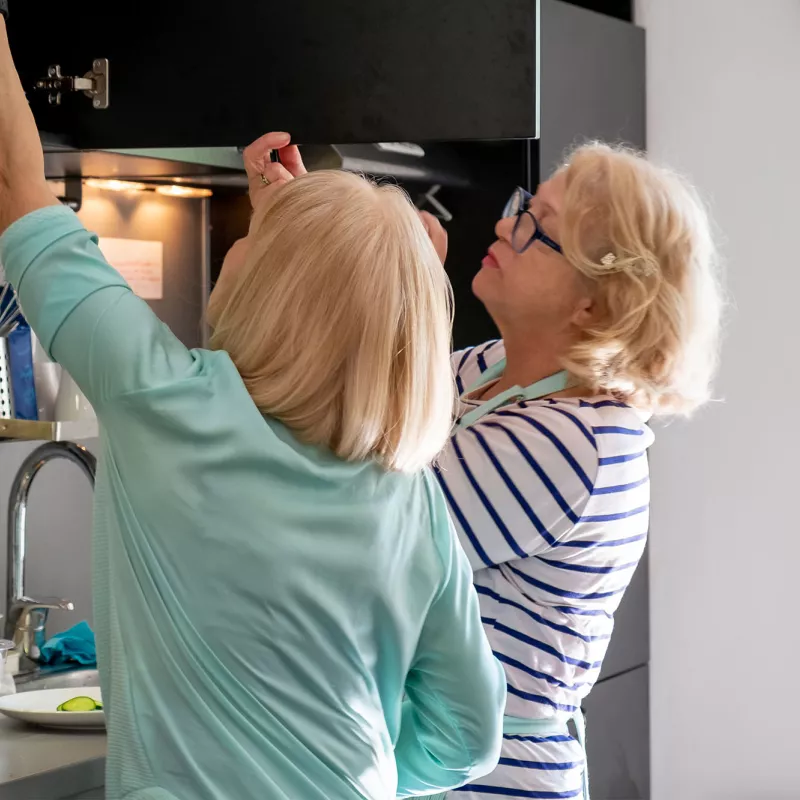 A Couple of Friends Get Ingredients From a Cabinet in the Kitchen as the Duo Prepares to Cook.