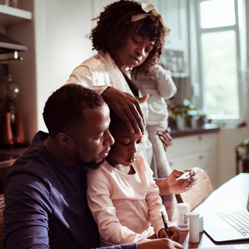 A Family Huddles Around a Laptop to Participate in a Video Visit with a Physician.