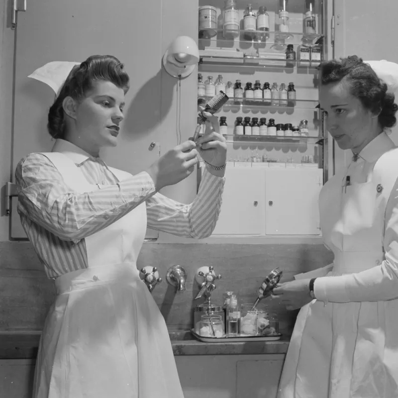 A Historical Photo of Two Nurses Drawing a Syringe. 
