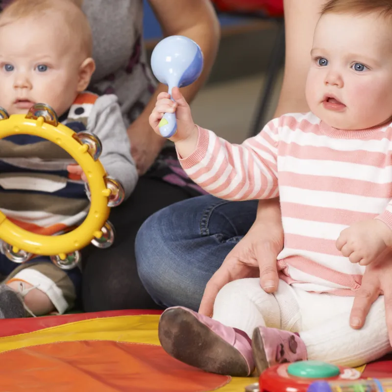 Two infants seated on the, held by their parents, holding baby instruments