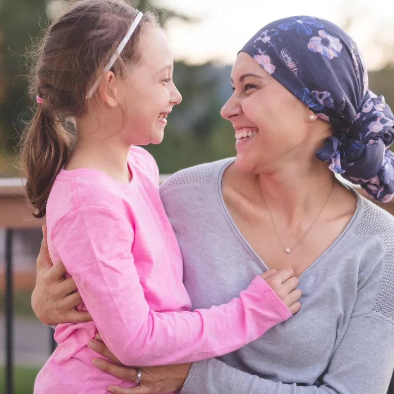 A mother and cancer survivor is sitting, with one arm around her daughter.