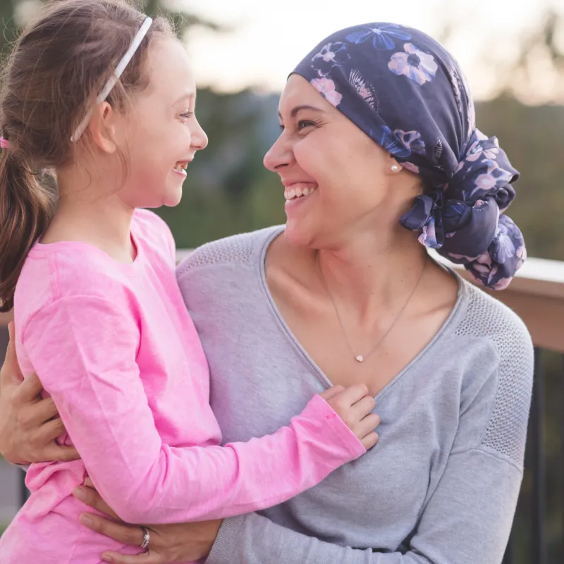 A mother and cancer survivor is sitting, with one arm around her daughter.