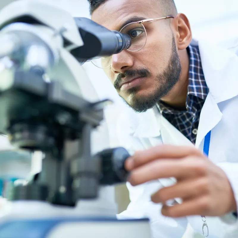 Man looking into a microscope to analyze the results of a clinical trial.