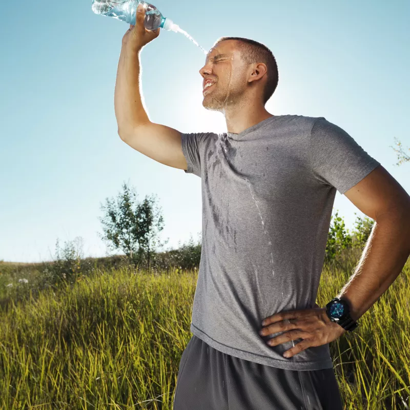 A man outside, post run, squirting water on his face