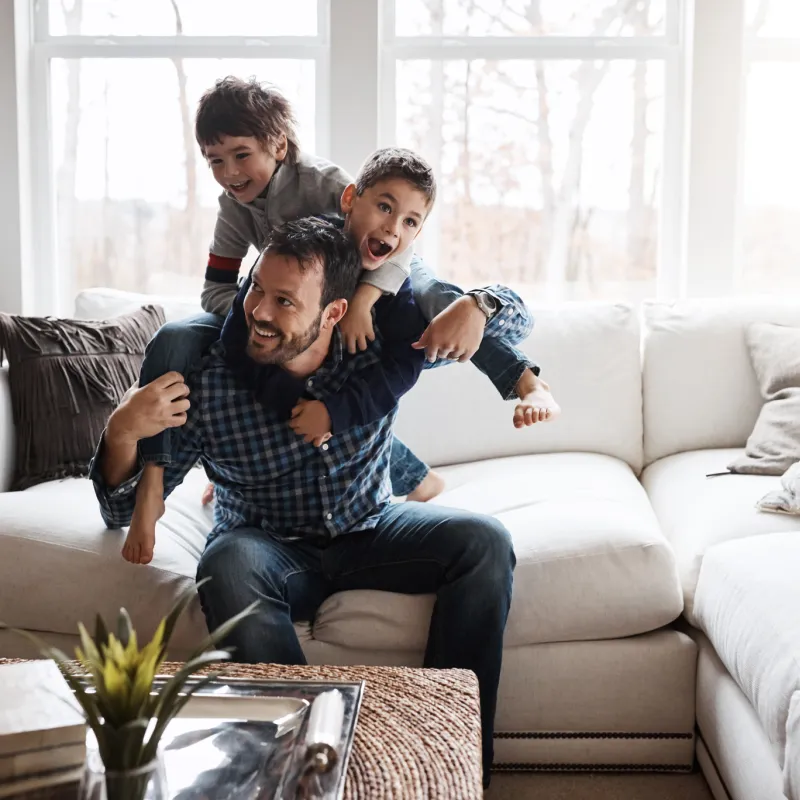 A father and his two sons playing on the sofa of their living room.