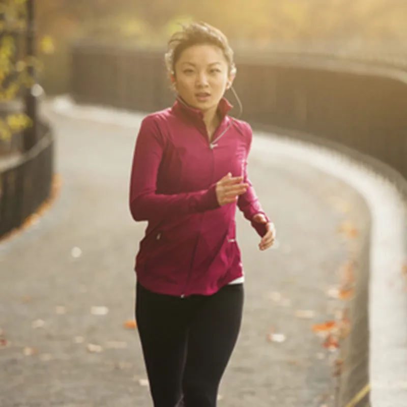 A young Asian woman jogs in the park on a fall afternoon.