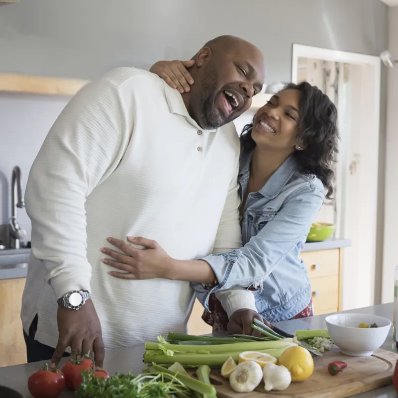 A couple shares a sweet moment as they prepare vegetables in their kitchen