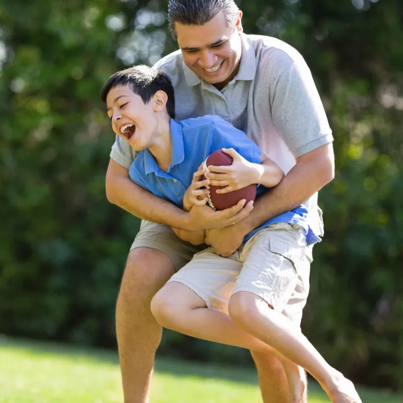 A father and son play football outdoors.