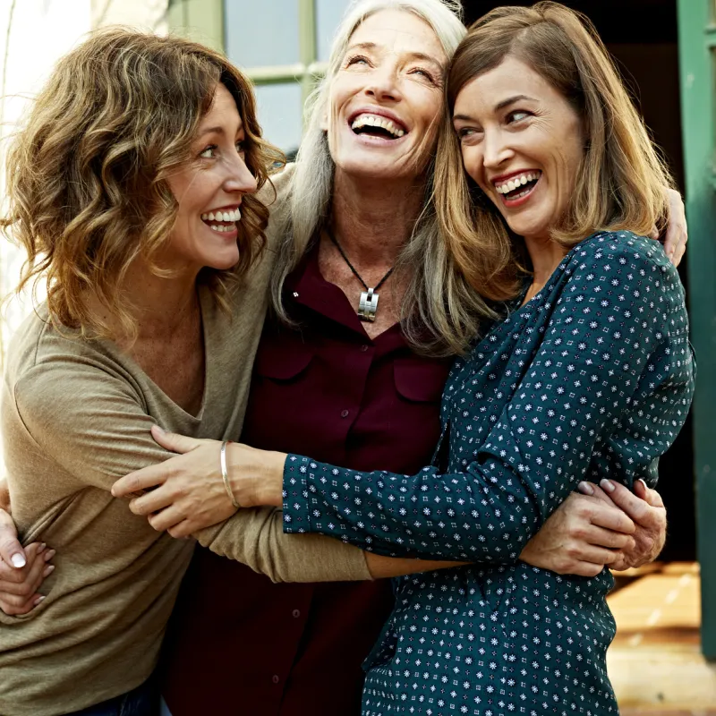 Three women celebrate their health by hugging each other.