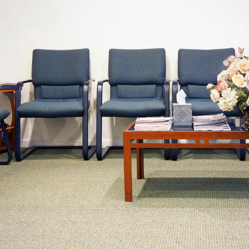 Hospital waiting room with blue chairs and a brown coffee table displaying flowers.