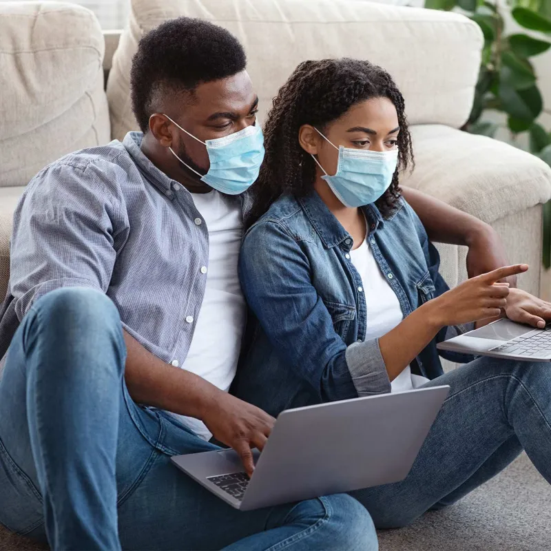 A couple wearing masks using their computers.