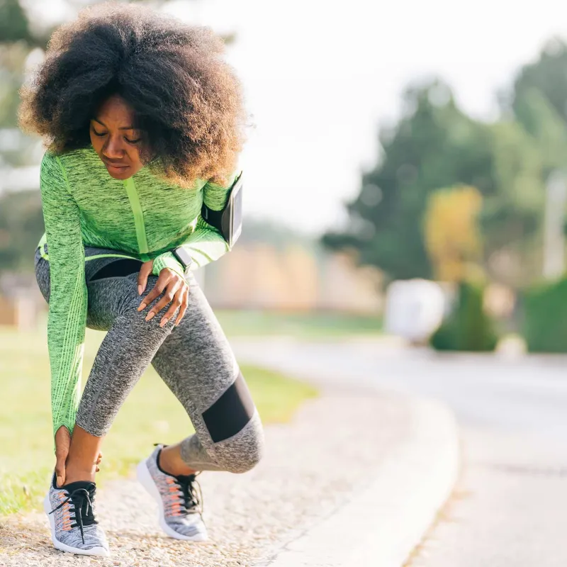 A woman checking her ankle during her run.