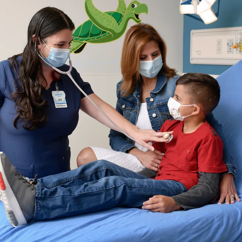 Nurse checking child's heartbeat at AdventHealth Fish Memorial Pediatric ER while his mother stands nearby.