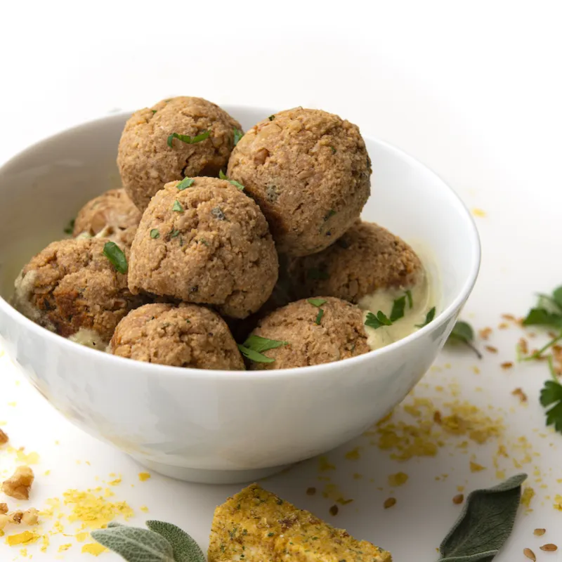 White bowl of no-meat balls with leaf garnishes on white counter