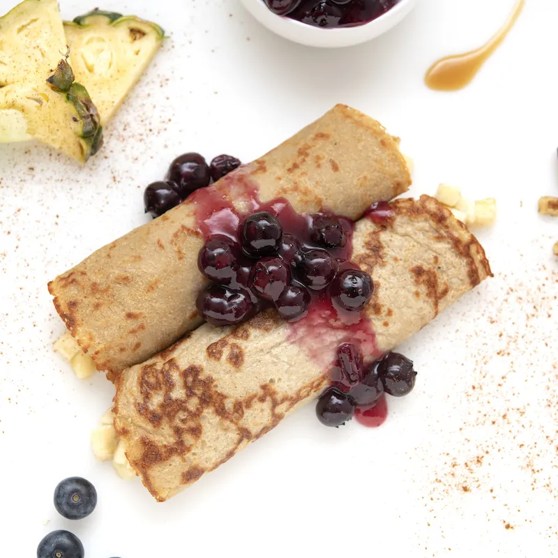 Two crepes covered with blueberry sauce next to pineapple garnish