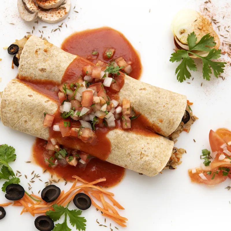 Two enchiladas with sauce and parsley, carrot, and olive garnishes