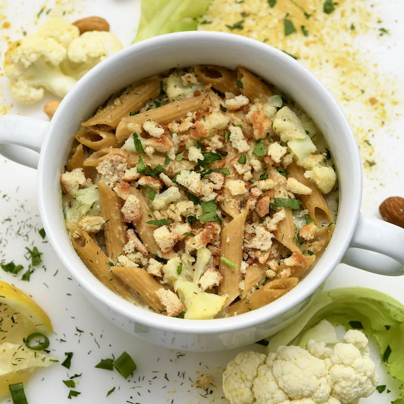 White bowl filled with cauliflower-pasta next to garnishes