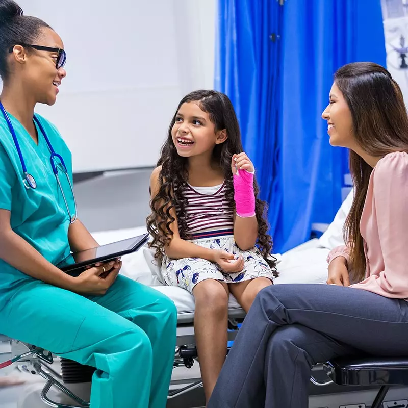 Child with a cast on her arm is sitting with a doctor and her mother