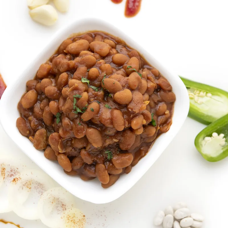 White bowl of baked beans with jalapeño garnish.