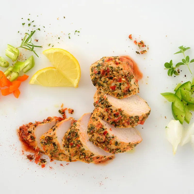 a sliced, chicken breast, surrounded by herbs, lemon, and veggies