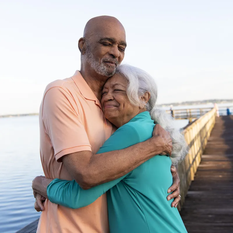 A couple standing on a pier by the lake hugging each other