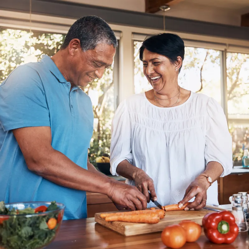 A couple cutting up carrots for a salad while in a kitchen.
