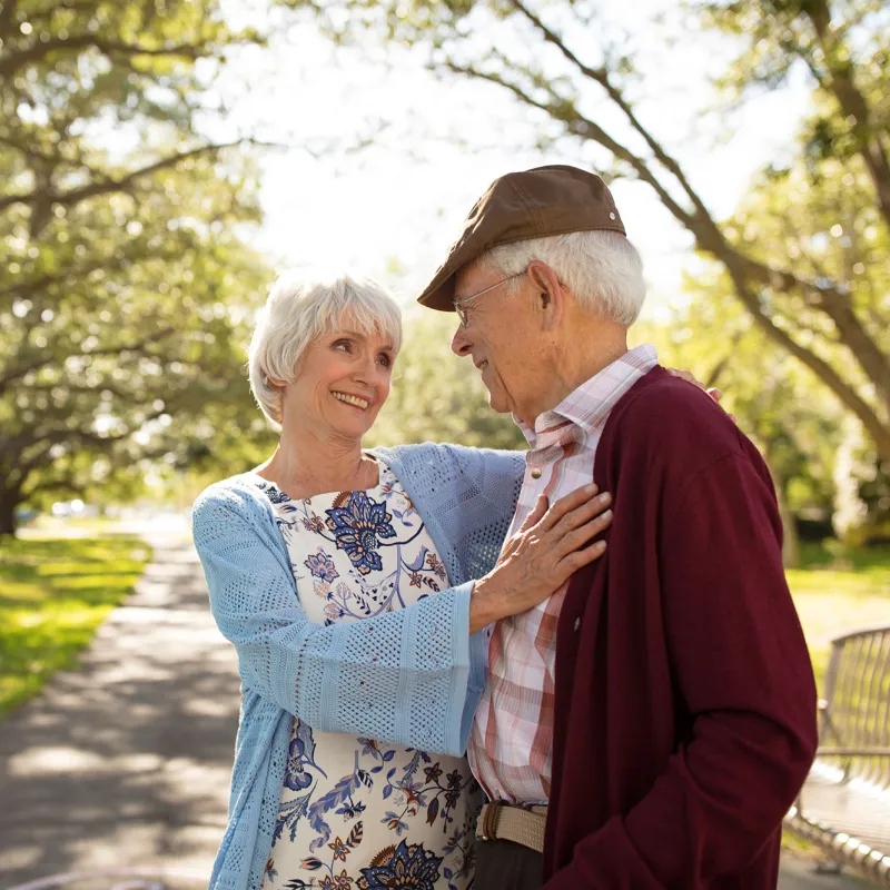 An elderly couple hugging each other at the park. 