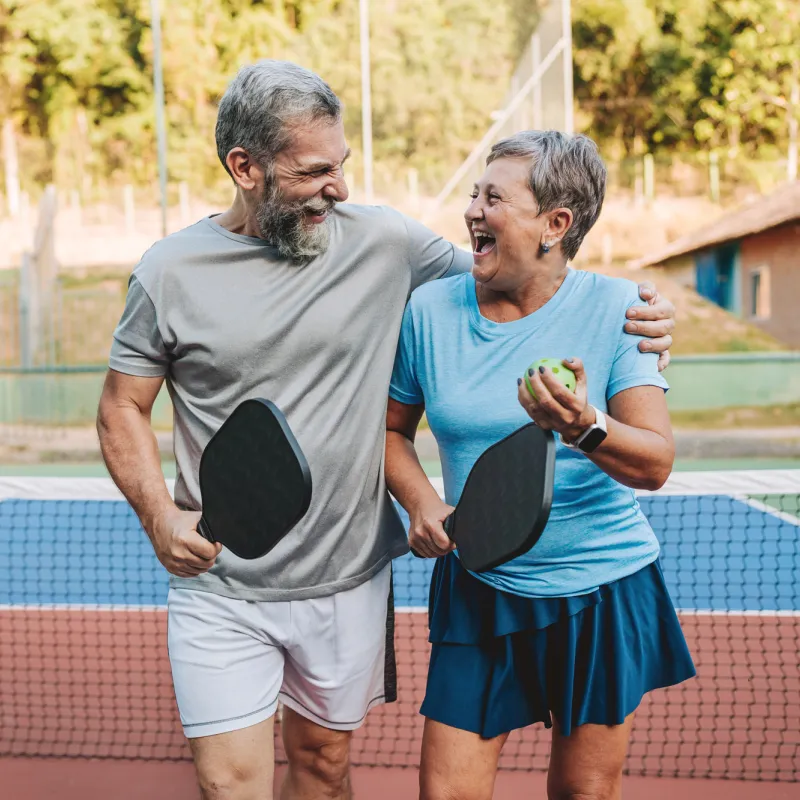 An older couple at an outdoor pickleball court together.
