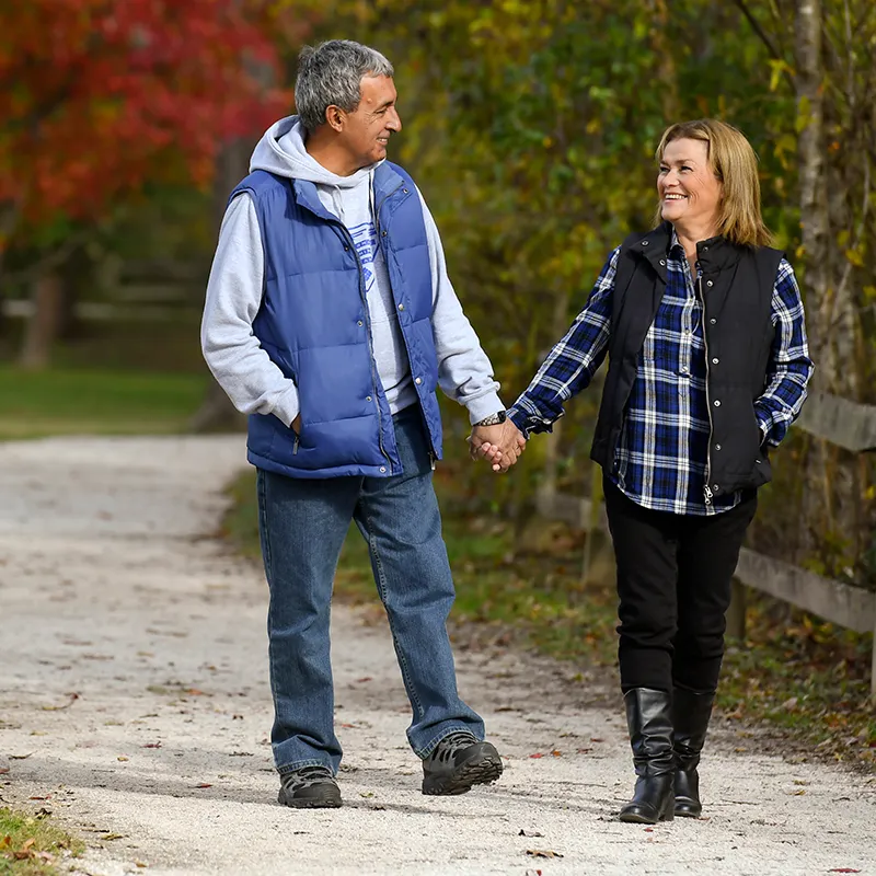 Couple walking down a path outdoors in the fall holding hands.