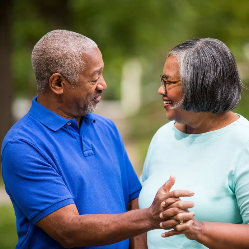 An elderly couple, enjoying each other company  while grabbing hands in the park. 