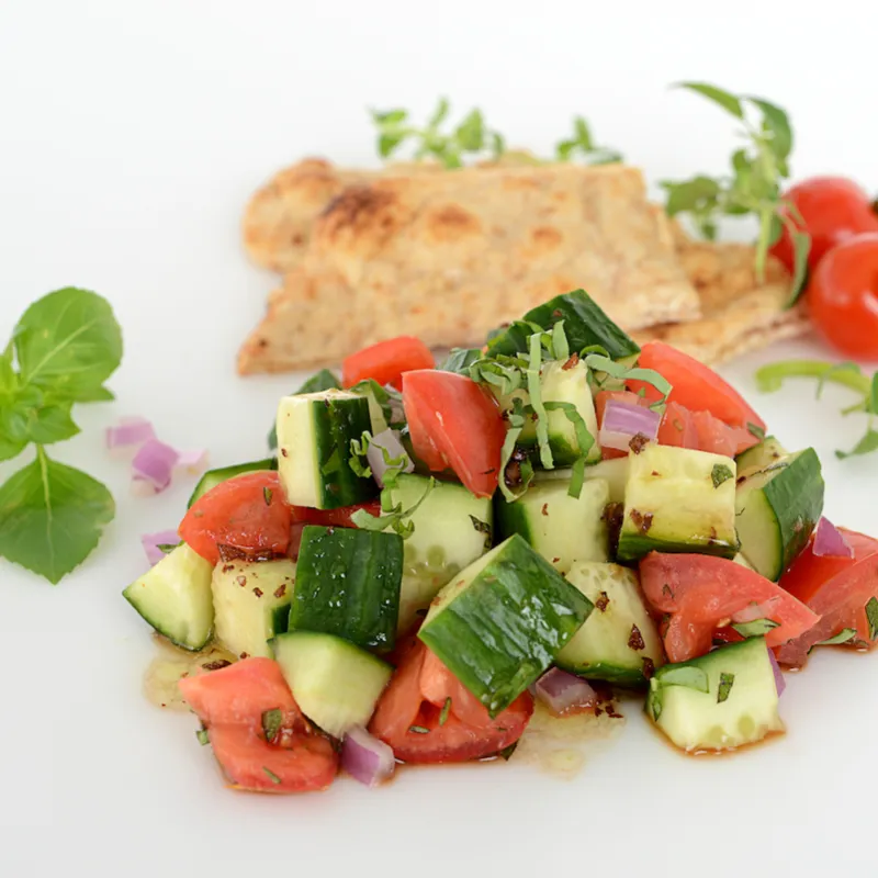 Mound of cucumber salad with pita and tomato garnishes