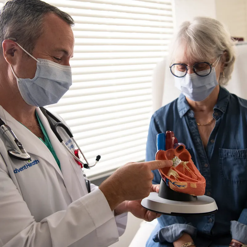 Doctor showing a woman patient a heart model while both wear masks.