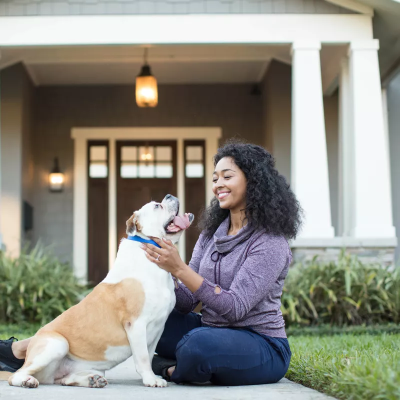 Women petting her dog outside her house.