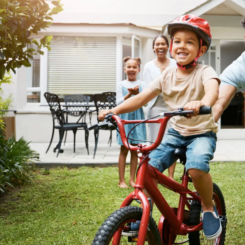 Family teaching son to ride bike in yard