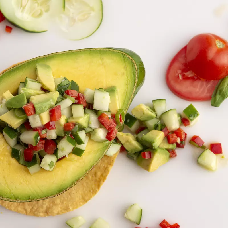 Half an avocado filled with avocado salsa on a white surface