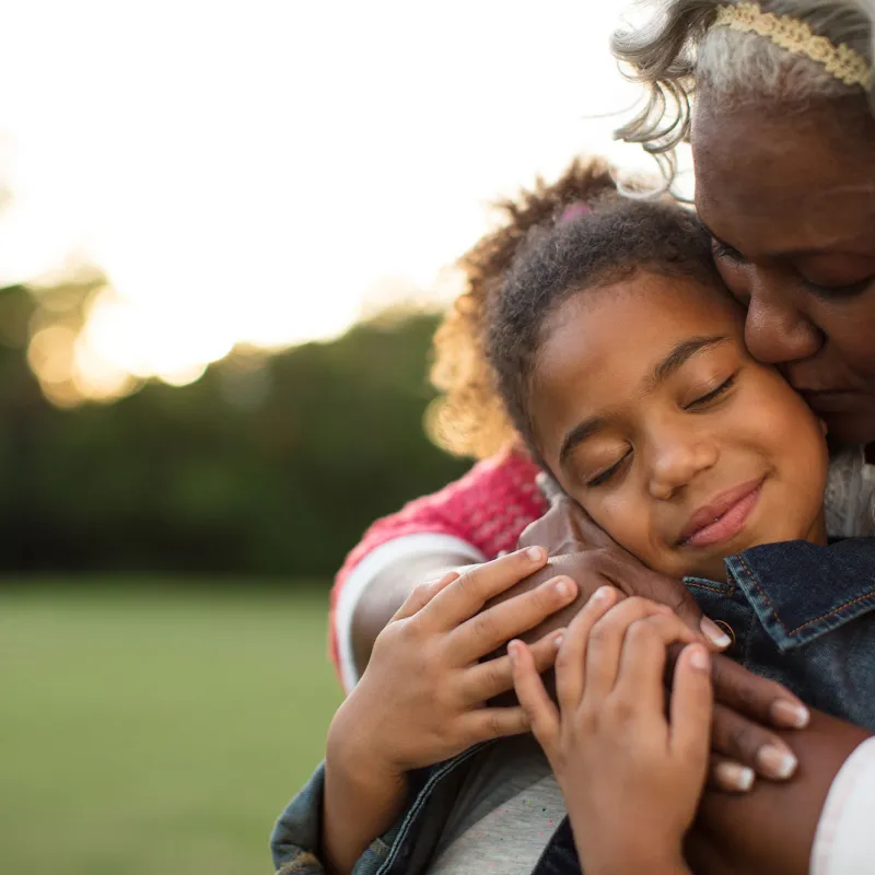 A grandmother hugging her grand-daughter at the park.