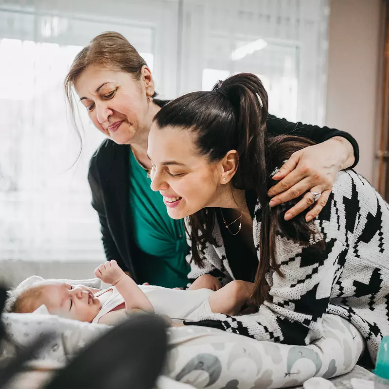 Grandmother and mother smiling at a baby laying on a bed.