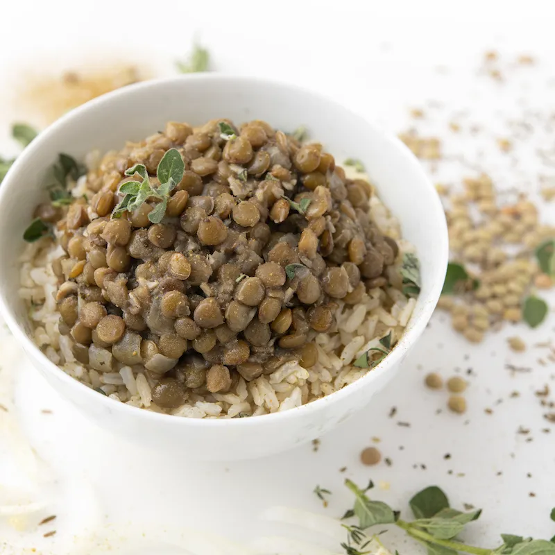 Bowl of lentils and rice on white surface with green garnish