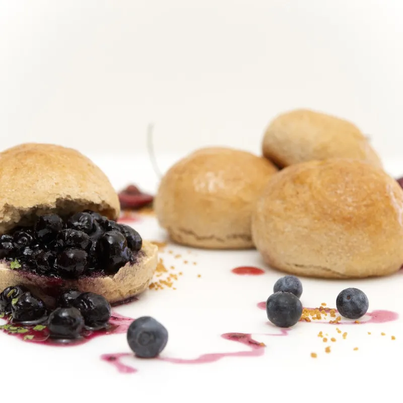 four fresh baked rolls, one covered in blueberries with a fruit syrup