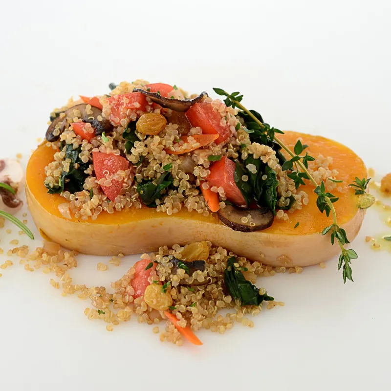 Quinoa, mixed with plum tomatoes, Swiss chard and mushrooms, placed in the center of a butternut squash half