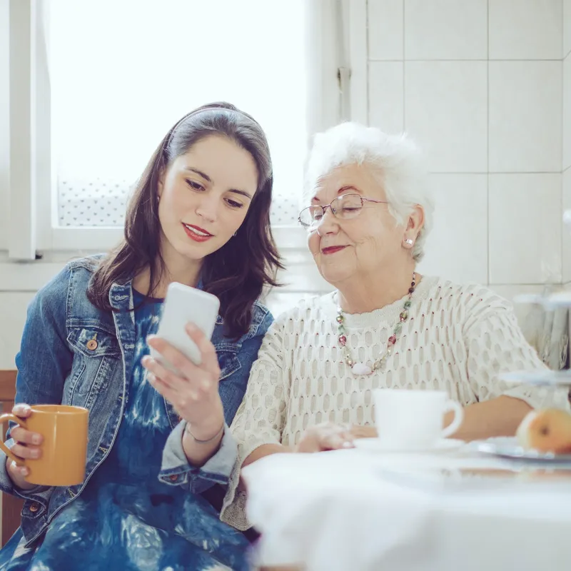 A daughter and her mom sitting at the dining table while looking at the cell phone