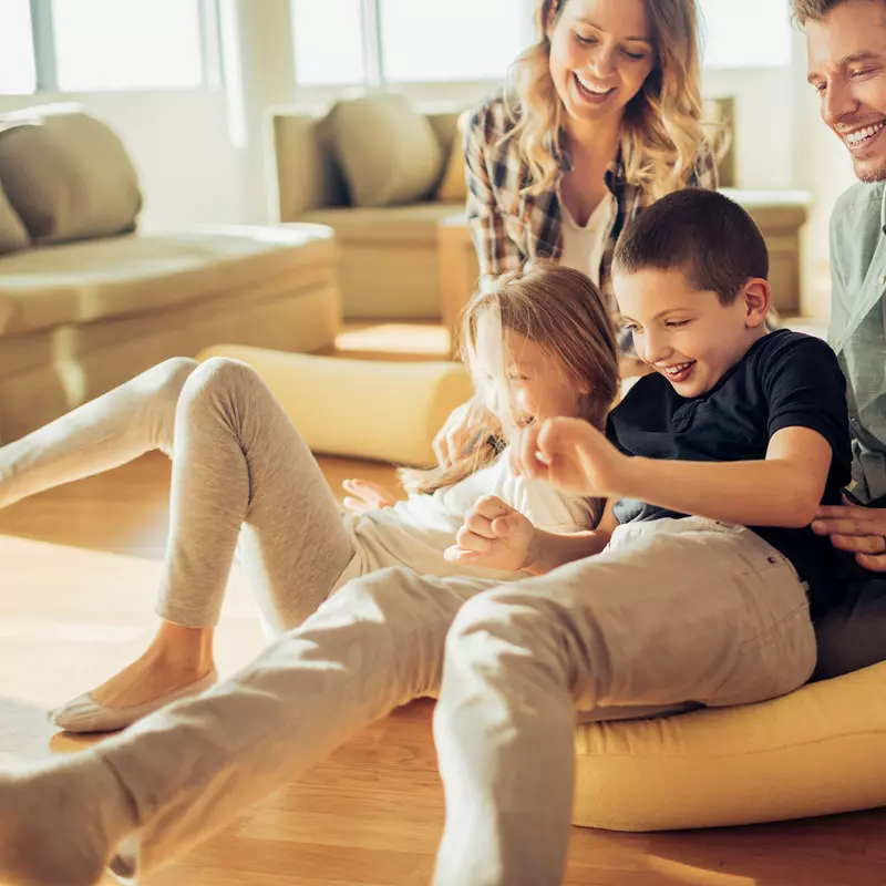 Family playing and laughing together in a sun filled living room of their house.